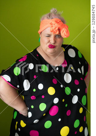 Plus size woman in vibrant polka dot outfit making a comic shrug gesture with outstretched hands and amusing expression. Plus size woman in vibrant polka dot outfit making a comic shrug gesture with outstretched hands and amusing expression. 129884745
