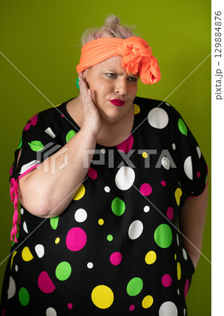 Plus size woman in vibrant polka dot outfit making a comic shrug gesture with outstretched hands and amusing expression. Plus size woman in vibrant polka dot outfit making a comic shrug gesture with outstretched hands and amusing expression. 129884876