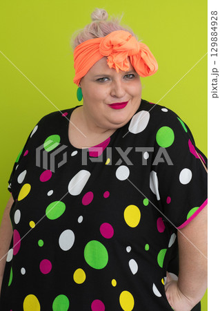 Plus size woman in vibrant polka dot outfit making a comic shrug gesture with outstretched hands and amusing expression. Plus size woman in vibrant polka dot outfit making a comic shrug gesture with outstretched hands and amusing expression. 129884928