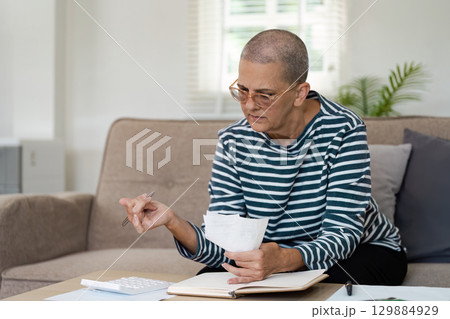 Senior Woman Planning Retirement Finances at Home with Documents and Calculator for Future Security and Comfort 129884929