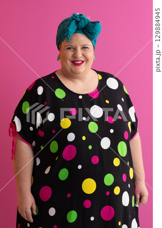 Colorful expressive big size woman posing in polka dot dress on pink background Colorful expressive big size woman posing in polka dot dress on pink background 129884945