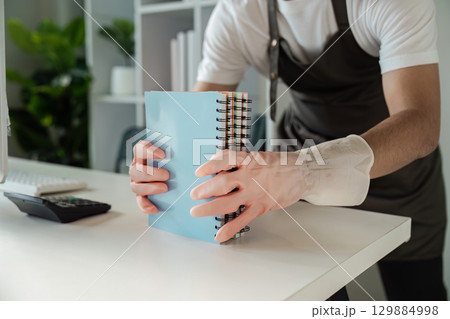 Person Cleaning Desk with Gloves and Organizing Notebooks in a Modern Office Environment 129884998