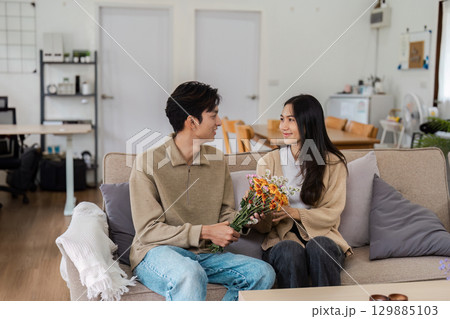 Happy Couple Relaxing on Sofa with Flowers, Embracing Love and Togetherness in a Cozy Home Setting Happy Couple Relaxing on Sofa with Flowers, Embracing Love and Togetherness in a Cozy Home Setting 129885103