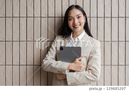Confident Businesswoman Holding Tablet Against Modern Textured Wall in Professional Attire 129885207