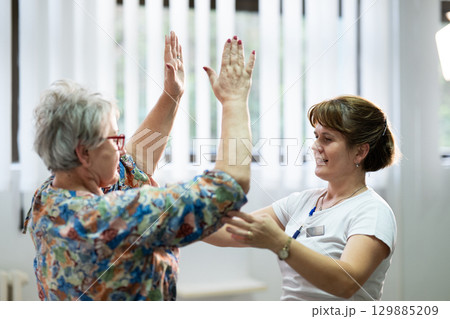 Senior Physical Therapy Session.Senior woman doing physical exercises with the help of a smiling therapist. Concept of elderly rehabilitation and movement recovery. Senior Physical Therapy Session.Senior woman doing physical exercises with the help of a smiling therapist. Concept of elderly rehabilitation and movement recovery. 129885209