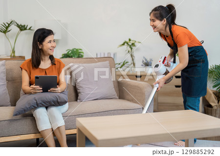 Professional Housekeeper Performing Cleaning Tasks in a Modern Home Environment with Vacuum and Smiling Client Professional Housekeeper Performing Cleaning Tasks in a Modern Home Environment with Vacuum and Smiling Client 129885292