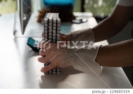 Person Wearing Gloves Organizing Notebooks on a Clean Desk in a Modern Office Environment with Natural Light Person Wearing Gloves Organizing Notebooks on a Clean Desk in a Modern Office Environment with Natural Light 129885334