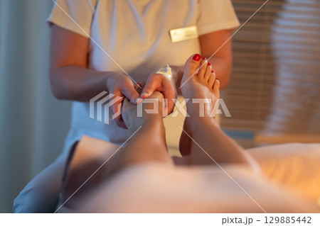 Foot Massage Therapy in a Relaxing Spa Setting. A professional massage therapist in a white uniform provides a soothing foot massage to a client in a calm and serene spa environment Foot Massage Therapy in a Relaxing Spa Setting. A professional massage therapist in a white uniform provides a soothing foot massage to a client in a calm and serene spa environment 129885442