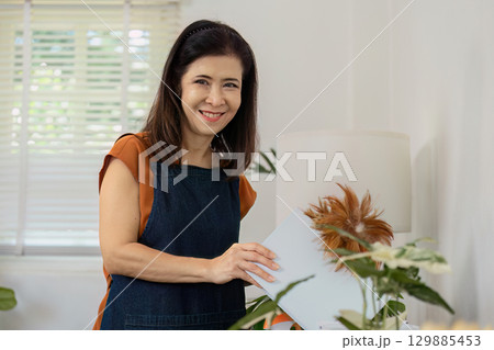 Smiling Woman in Apron Engaged in Home Cleaning with Natural Light and Indoor Plants for a Fresh and Inviting Atmosphere Smiling Woman in Apron Engaged in Home Cleaning with Natural Light and Indoor Plants for a Fresh and Inviting Atmosphere 129885453