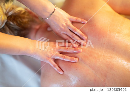 Relaxing Back Massage in a Spa Setting. A professional massage therapist in a blue uniform provides a relaxing back massage to a client lying on a massage table. Relaxing Back Massage in a Spa Setting. A professional massage therapist in a blue uniform provides a relaxing back massage to a client lying on a massage table. 129885491