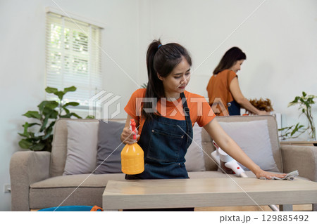 Young Women Cleaning a Modern Living Room with Cleaning Supplies and Tools in a Bright, Tidy Home Environment 129885492