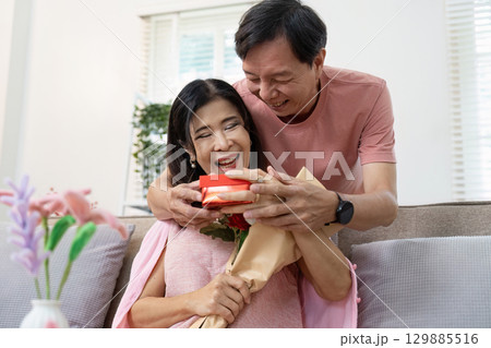 Joyful Senior Couple Celebrating Valentine's Day with Gifts and Flowers in a Cozy Home Setting 129885516