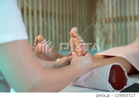 Foot Massage Therapy in a Relaxing Spa Setting. A professional massage therapist in a white uniform provides a soothing foot massage to a client in a calm and serene spa environment 129885517