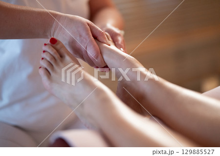 Foot Massage Therapy in a Relaxing Spa Setting. A professional massage therapist in a white uniform provides a soothing foot massage to a client in a calm and serene spa environment 129885527