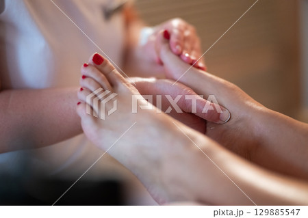 Foot Massage Therapy in a Relaxing Spa Setting. A professional massage therapist in a white uniform provides a soothing foot massage to a client in a calm and serene spa environment 129885547