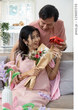 Elderly Couple Celebrating Valentine's Day with Flowers and Gifts in a Cozy Home Setting 129885550