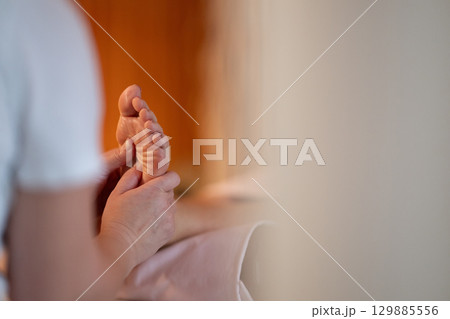 Foot Massage Therapy in a Relaxing Spa Setting. A professional massage therapist in a white uniform provides a soothing foot massage to a client in a calm and serene spa environment 129885556