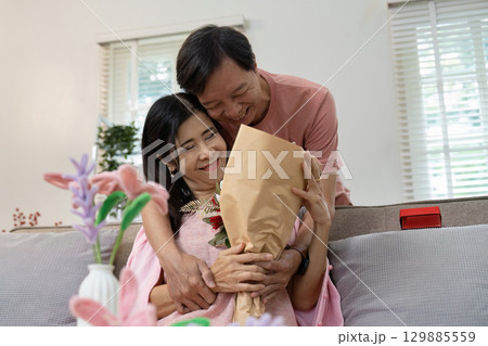 Romantic Valentine's Day Celebration with Happy Couple Embracing and Sharing a Bouquet of Flowers in Cozy Home Setting 129885559