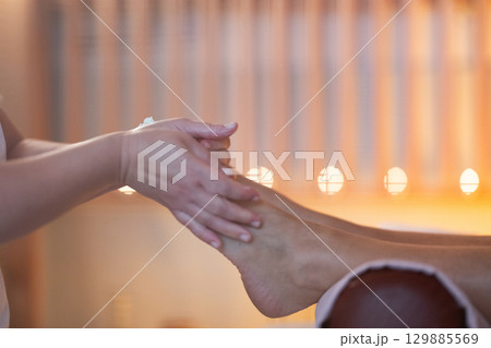 Foot Massage Therapy in a Relaxing Spa Setting. A professional massage therapist in a white uniform provides a soothing foot massage to a client in a calm and serene spa environment Foot Massage Therapy in a Relaxing Spa Setting. A professional massage therapist in a white uniform provides a soothing foot massage to a client in a calm and serene spa environment 129885569