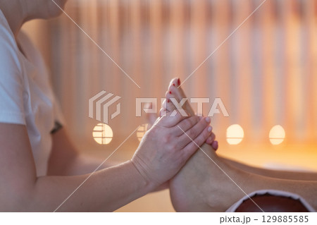 Foot Massage Therapy in a Relaxing Spa Setting. A professional massage therapist in a white uniform provides a soothing foot massage to a client in a calm and serene spa environment Foot Massage Therapy in a Relaxing Spa Setting. A professional massage therapist in a white uniform provides a soothing foot massage to a client in a calm and serene spa environment 129885585