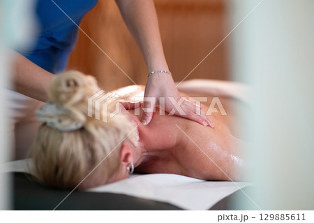 Relaxing Back Massage in a Spa Setting. A professional massage therapist in a blue uniform provides a relaxing back massage to a client lying on a massage table. 129885611