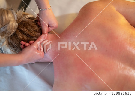 Relaxing Back Massage in a Spa Setting. A professional massage therapist in a blue uniform provides a relaxing back massage to a client lying on a massage table. Relaxing Back Massage in a Spa Setting. A professional massage therapist in a blue uniform provides a relaxing back massage to a client lying on a massage table. 129885616