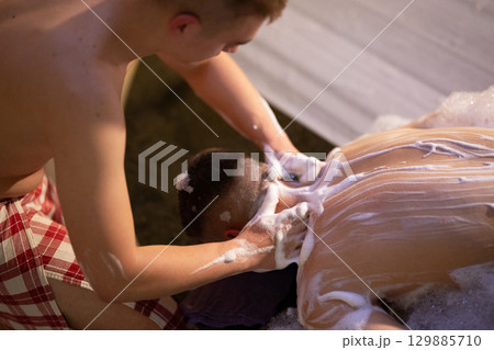 Back Massage with Foam.Therapist applying soap foam with hands on patient back during traditional bath ritual. 129885710
