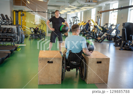 Rearview wheelchair athlete trains with personal coach. Injury rehab with weighted ball exercise 129885788