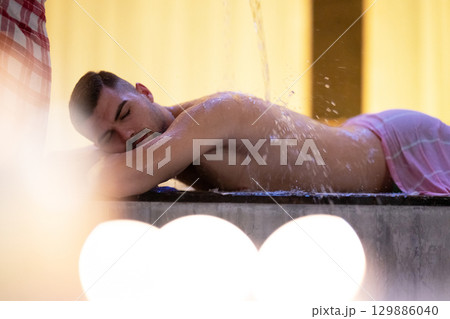 Man receiving water therapy inside a traditional Turkish hammam with ornate details. Man receiving water therapy inside a traditional Turkish hammam with ornate details. 129886040