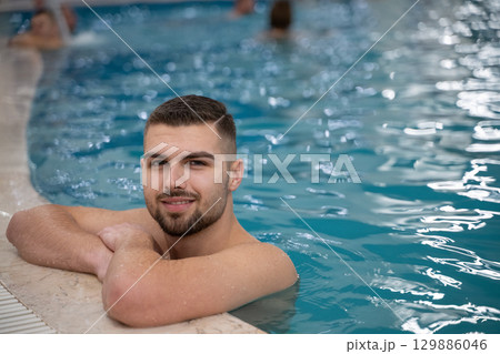 Man resting on the edge of a large indoor pool with a calm expression and relaxed posture. 129886046