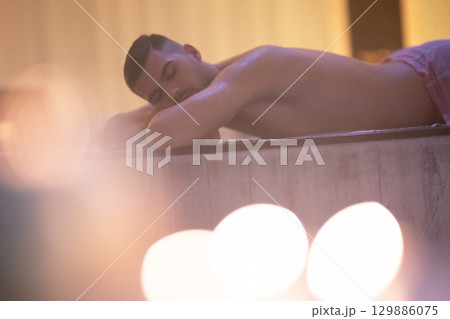 Man relaxing on a marble platform inside a Turkish bath with warm lighting. 129886075