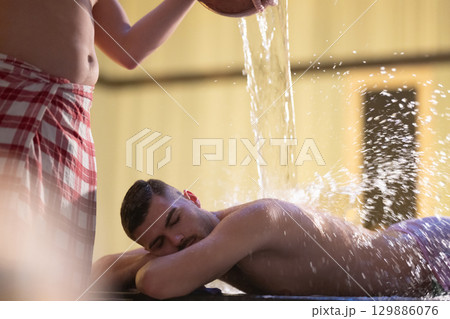 Man receiving water therapy inside a traditional Turkish hammam with ornate details. Man receiving water therapy inside a traditional Turkish hammam with ornate details. 129886076