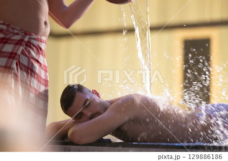 Man receiving water therapy inside a traditional Turkish hammam with ornate details. 129886186