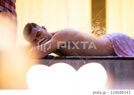 Man receiving water therapy inside a traditional Turkish hammam with ornate details. 129886341