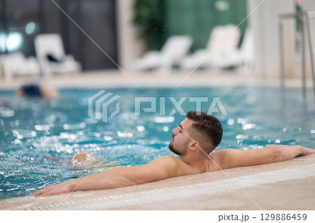 Man floating peacefully in warm spa water with eyes closed and arms outstretched on the edge of the pool. Man floating peacefully in warm spa water with eyes closed and arms outstretched on the edge of the pool. 129886459