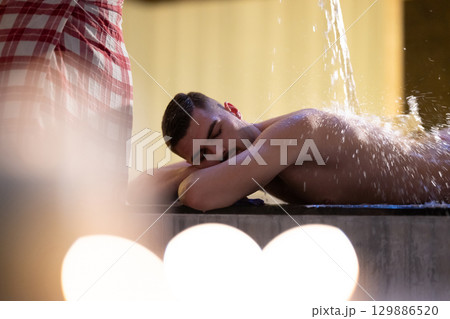 Man receiving water therapy inside a traditional Turkish hammam with ornate details. 129886520