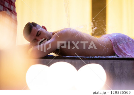 Man receiving water therapy inside a traditional Turkish hammam with ornate details. Man receiving water therapy inside a traditional Turkish hammam with ornate details. 129886569