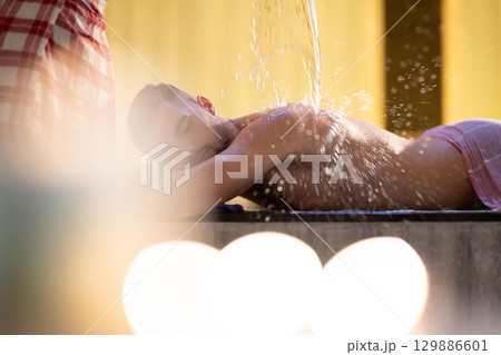 Man receiving water therapy inside a traditional Turkish hammam with ornate details. 129886601