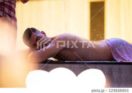 Man receiving water therapy inside a traditional Turkish hammam with ornate details. Man receiving water therapy inside a traditional Turkish hammam with ornate details. 129886603