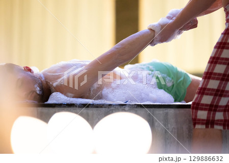Hand Foam Therapy. Attendant gently washing patient hands with foamy soap in traditional bath setting. 129886632
