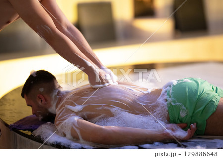 Back Massage with Foam.Therapist applying soap foam with hands on patient back during traditional bath ritual. 129886648