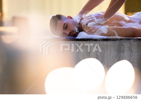 Back Massage with Foam.Therapist applying soap foam with hands on patient back during traditional bath ritual. Back Massage with Foam.Therapist applying soap foam with hands on patient back during traditional bath ritual. 129886656