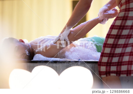 Hand Foam Therapy. Attendant gently washing patient hands with foamy soap in traditional bath setting. 129886668