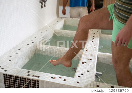 Man Stepping in Spa Water Walkway.Close up of a mans legs as he steps into tiled spa therapy pools for a hydrotherapy session. Man Stepping in Spa Water Walkway.Close up of a mans legs as he steps into tiled spa therapy pools for a hydrotherapy session. 129886790