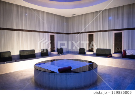 Modern hammam steam room with a central round stone massage table and stylish decor. 129886809