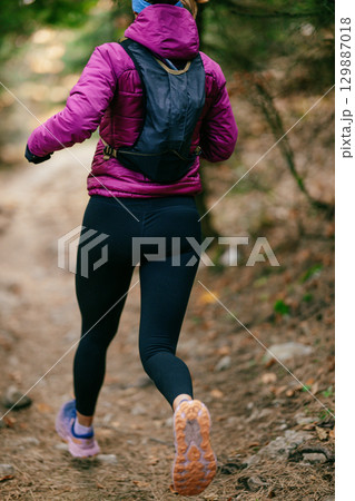 Determined Female Athlete Running with Focus Through a Dense Pine Forest, Embracing Strength and Nature 129887018