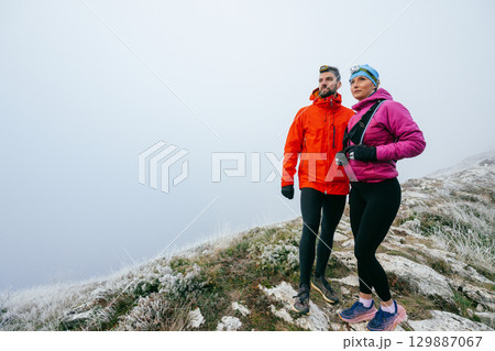 Hikers Posing on Foggy Mountain Top.Portrait of two hikers posing together on a foggy mountain top wearing outdoor gear. Hikers Posing on Foggy Mountain Top.Portrait of two hikers posing together on a foggy mountain top wearing outdoor gear. 129887067