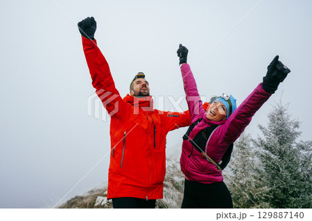 Victory Celebration at the Summit.Two hikers raise their arms in celebration at the mountain summit, showing joy and success after a long night trek. 129887140