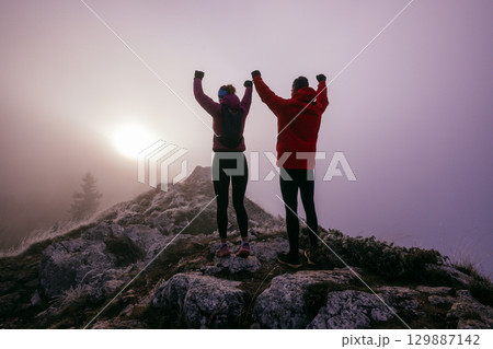 Two Hikers Celebrating on Rocky Peak.Couple hikers raising fists on rugged mountain ridge at sunrise. Two Hikers Celebrating on Rocky Peak.Couple hikers raising fists on rugged mountain ridge at sunrise. 129887142