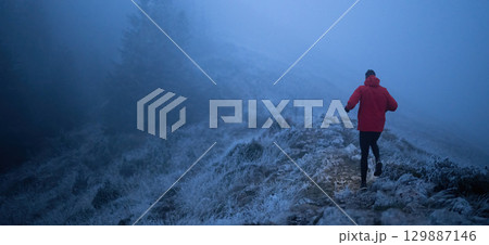 Balancing on the Mountain Trail at Dusk.A lone hiker balances on a rocky mountain trail during early morning or dusk, with a headlamp lighting the misty path. Balancing on the Mountain Trail at Dusk.A lone hiker balances on a rocky mountain trail during early morning or dusk, with a headlamp lighting the misty path. 129887146